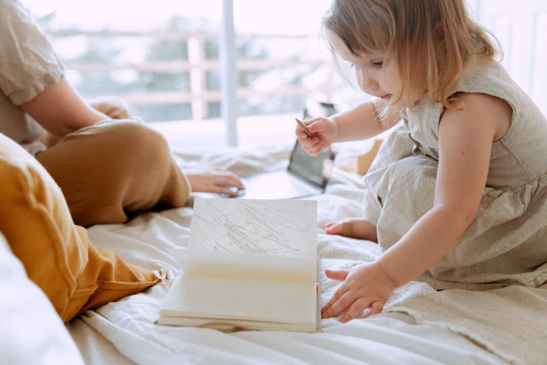 Ein kleines Mädchen hat ein Stift in der Hand und ein bemaltes Buch vor sich